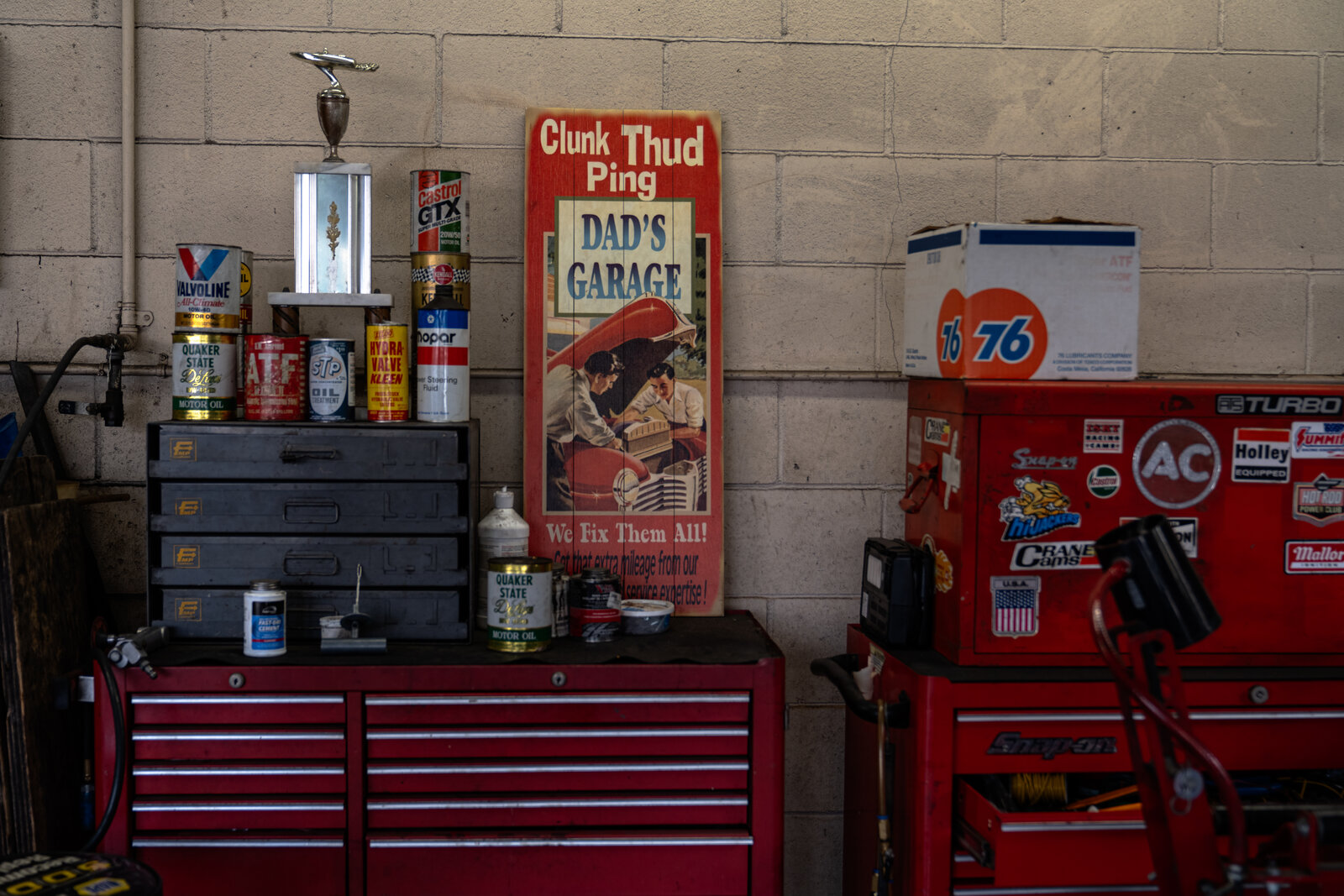 A trophy and vintage motor oil cans on a shelf next to a sign reading Dad's Garage