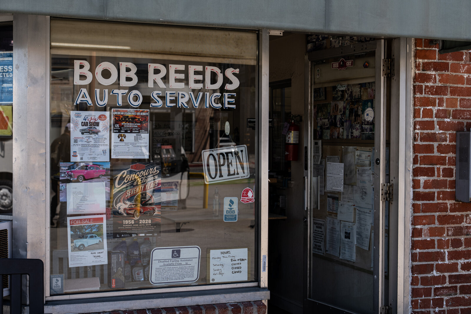 Bob Reed's Auto Service hand-painted window lettering, with posted hours and an OPEN sign